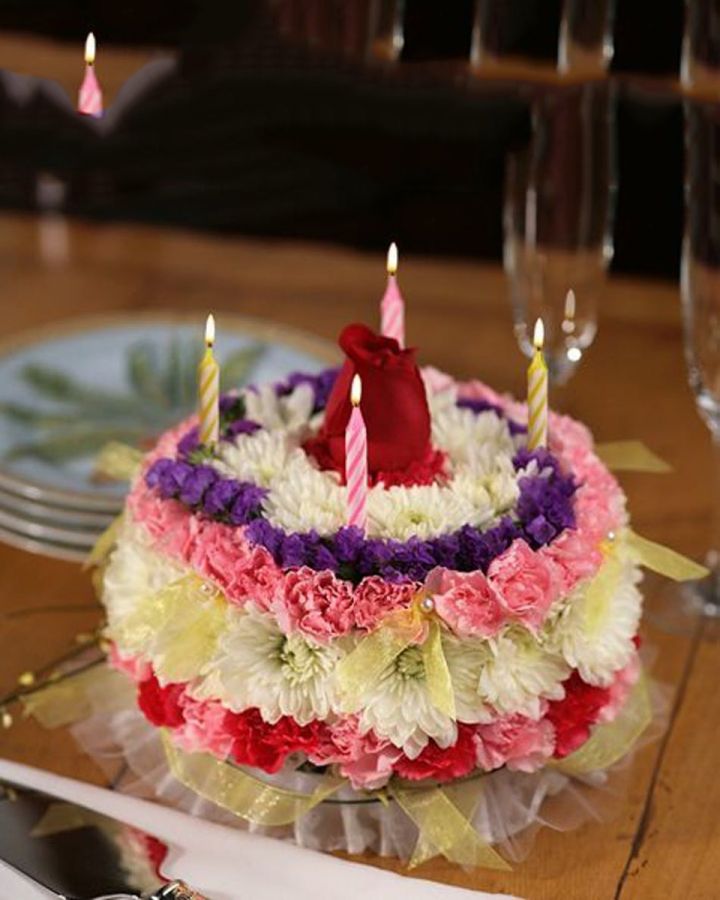 Flowering Birthday Cake Flowering Birthday Cake-Standard Our signature floral birthday cake may look good enough to eat... but we suggest you don't! It's actually crafted  Our signature floral birthday cake may look good enough to eat... but we suggest you don't! It's actually crafted from fresh, brightly colored flowers such as mini carnations and daisy poms in shades of white, red, pink and purple, topped with a beautiful, bright red rose! Cake is delivered with 4 candles. Plate not included. To ensure freshness, colors and varieties may vary.  
DELIVERY: Every order is hand-delivered direct to the recipient. These items will be delivered by us locally, or a qualified retail local florist.