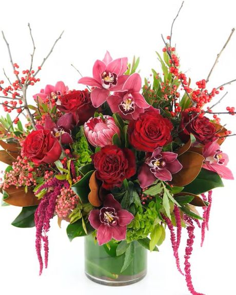 WINTER EXTRAVAGANZA-This lush design features the warm and rich colors of the season with luxurious red roses and winter textures made extra special by the addition of tropical orchid blooms, exotic protea, and hanging amaranthuS.- ARRANGEMENTS