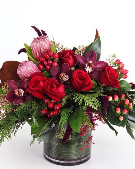 Winter Armth-Winter Warmth- This lush, low arrangement features the warm and rich colors of the season with red roses and winter textures made extra special by the addition of tropical orchid blooms and exotic protea-Christmas Arrangements