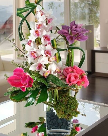 Caribbean Caress- white cymbidium orchid, lavender and pink calla lilies, pink roses, monstera and bear grass leaves, are arranged in a glass vase-Tropical Arrangement